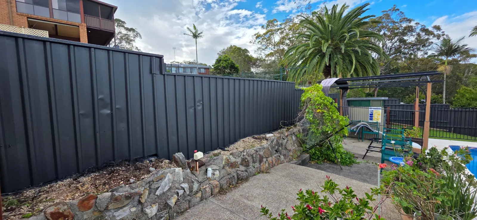 Colorbond fence above a stone retaining wall in Jewells, painted Colorbond Monument