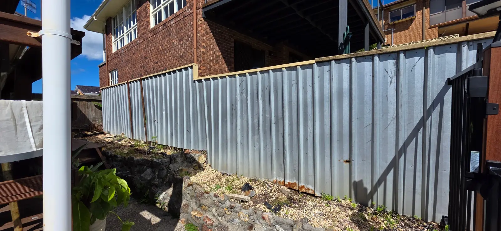 Bare galvanised fence panels beside a brick house before painting